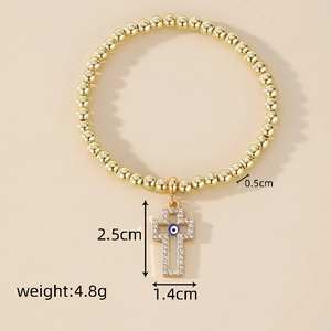 Detailed view of gold beaded bracelet with crystal cross charm and blue evil eye inlay