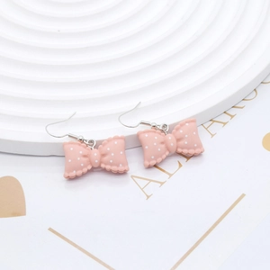 Cute pink resin bow earrings with white polka dots and silver hooks on a display stand