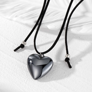 Détail du pendentif cœur noir sur cordon avec perle métallique sur fond blanc
