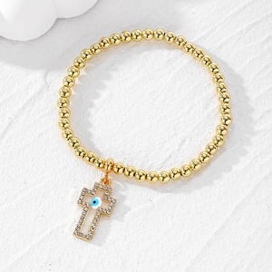 Detailed macro of gold beaded bracelet featuring a diamond-encrusted evil eye cross charm