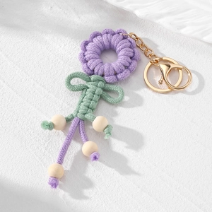 Detail eines handgewebten lila Blumen-Schlüsselanhängers mit Holzperlen und Goldkarabiner