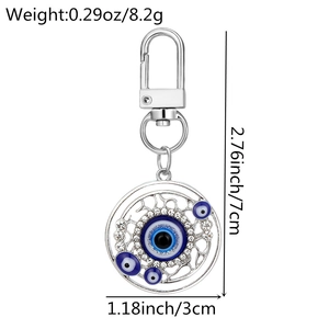 Macro shot of silver evil eye keychain with blue stones and dimensions listed