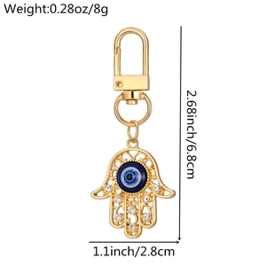 Detailed view of Hamsa Hand and Evil Eye keychain with white crystals and golden finish