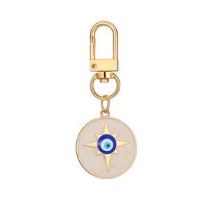 Detail of a golden evil eye keychain featuring a white enamel disc and octagonal star charm
