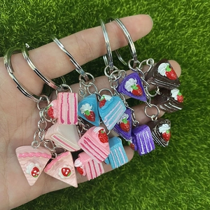 Close-up of colorful resin strawberry cake slice keychains held over green grass