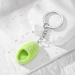 Detail view of a green fuzzy mini slipper keychain with silver metal ring and soft texture