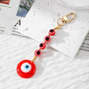 Red Evil Eye beaded keychain with resin charms and golden lobster clasp on white pedestal