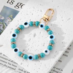 Handmade Evil Eye beaded keychain with turquoise and gold accents on a stone background