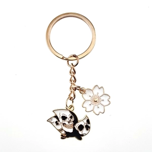 Detail of gold metal keychain with stacked skull charms and white enamel cherry blossom
