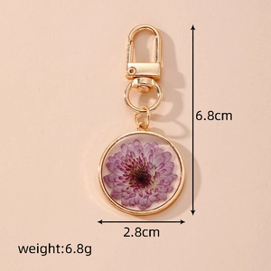 Detail of round dried flower keychain with purple daisy and gold metal clasp