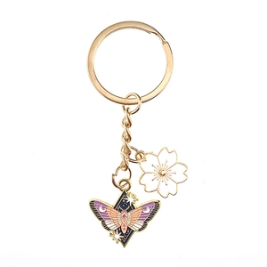 Golden keychain with purple enamel butterfly and white cherry blossom charm on white background