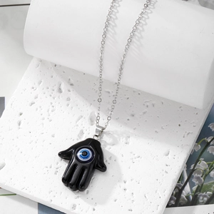 Macro shot of Hamsa hand pendant with blue evil eye on white marble background