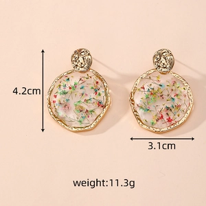Detail view of round resin earrings with dried flowers and gold textured metal frame