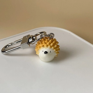 Close-up of a cute resin hedgehog keychain with silver metal clasp on a white round base