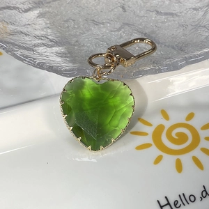 Exquisite green faceted crystal heart keychain with golden metal clasp on a ceramic tray
