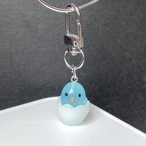 Macro view of a cute blue chick hatching from an eggshell with a silver lobster clasp