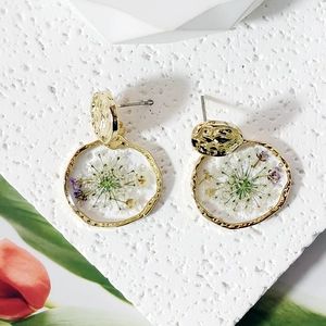Detail of irregular gold earrings with real white and purple dried flowers in resin