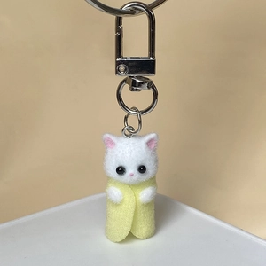 Detailed macro view of a white flocked kitten keychain in a yellow felt wrap with silver clasp