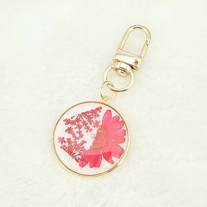 Macro shot of clear resin pendant featuring pink dried daisy flowers on white faux fur