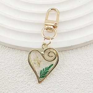 Detail of heart-shaped gold keychain with white dried flowers and green leaves in resin