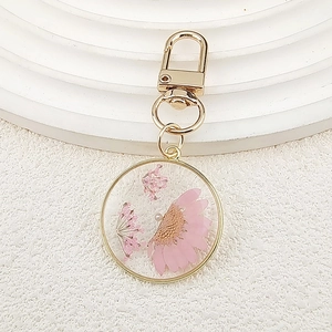 Detailed close-up of a pink daisy preserved in a clear resin pendant with gold trim