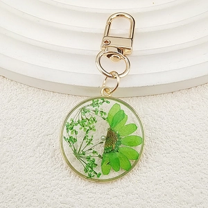 Detailed macro view of a gold resin keychain featuring green dried flowers and a pearl