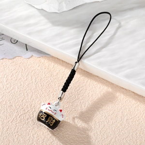 Close-up of Maneki-Neko bell pendant with black rope strap on white textured tray
