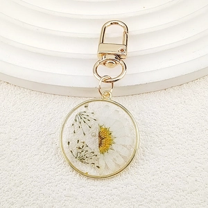Macro shot of circular resin keychain with white daisy dried flowers and gold frame