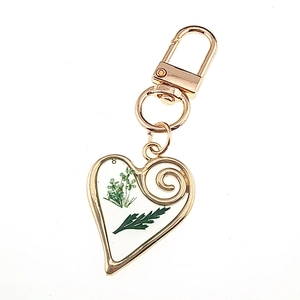 Detail of heart-shaped resin keychain with real green dried flowers and gold metal frame
