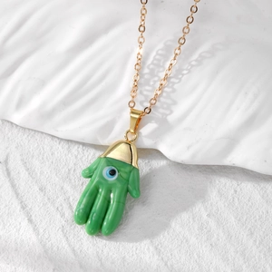 Detailed close-up of a green Hamsa pendant necklace with a blue evil eye on white ceramic