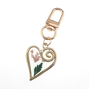 Macro shot of gold heart keychain with real pink dried flowers and green leaf in resin