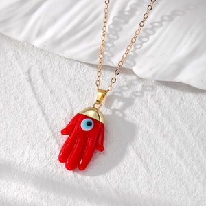 Detailed close-up of red Hamsa hand pendant with evil eye on a white stone background