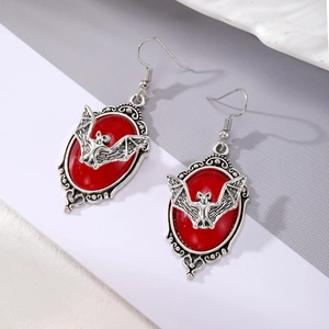 Détail de boucles d'oreilles gothiques chauve-souris avec pierre rouge et métal
