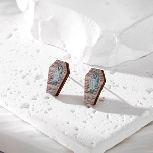 Detail of wooden coffin earrings with owl pattern on minimalist stone display