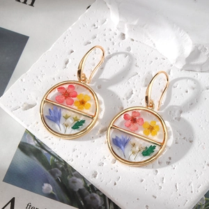 Detail of round resin earrings with real colorful dried flowers and gold metal hooks