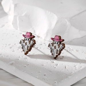 Ghost earrings with cow print and pink cowboy hat on textured white stone background