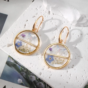 Detail of gold geometric earrings with blue and purple dried flowers in resin