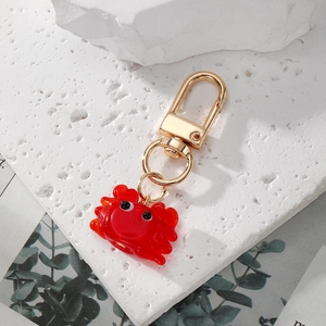 Porte-clés crabe rouge en résine avec boucle dorée sur un socle en pierre blanche