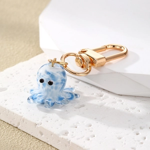 Blue and white glass octopus keychain with gold clasp on stone background