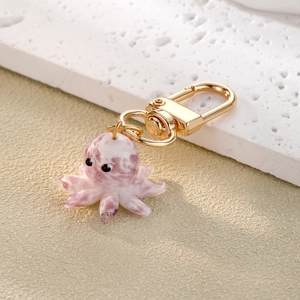 Pink glass octopus keychain with golden metal clasp on a textured stone background