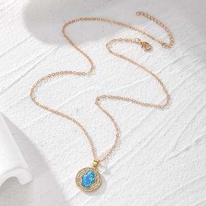 Goldene Hamsa-Halskette mit blauem Opal-Anhänger und Zirkonia-Rand auf weißem Stein