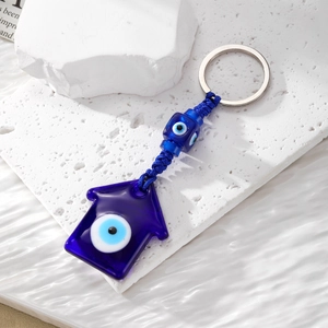 Detailed view of evil eye glass keychain with blue woven cord on white stone surface
