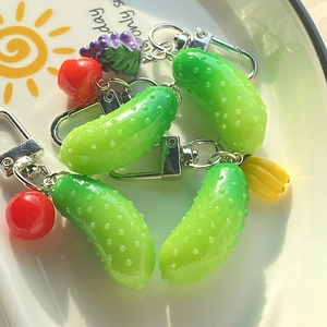 Close-up of resin cucumber pendants with fruit charms and silver metal clasps on a plate