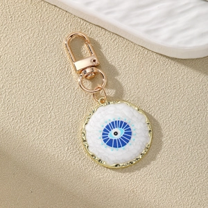 Ethnic style Evil Eye and gold heart keychain pendant with blue enamel on sandy background
