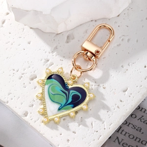 Vintage heart keychain with fluid enamel painting and pearl border on stone surface