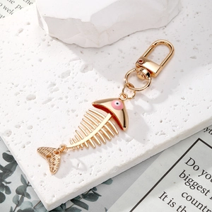 Golden fishbone keychain with evil eye detail on white stone textured background