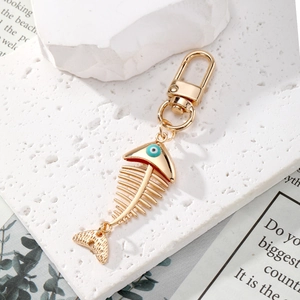 Golden fishbone keychain with blue evil eye bead on white stone texture background