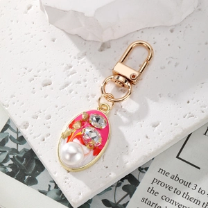 Vintage gold-plated oval keychain with pink enamel, crystals, and faux pearl on a stone slab