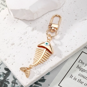 Golden fishbone keychain with blue evil eye charm on a stylish stone display pedestal