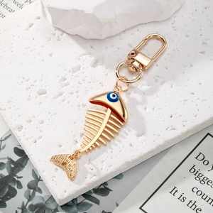 Detail view of golden alloy fishbone keychain with blue evil eye charm on stone surface